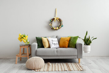 Comfortable sofa near light wall with Easter wreath in living room interior
