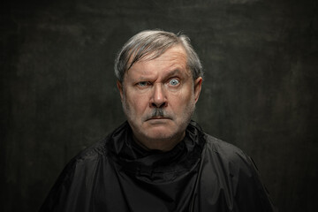 Portrait of angry senior man looking at camera isolated on dark vintage background. Concept of...