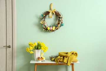 Table with beautiful tulips, knitted sweaters and stylish Easter decor near color wall
