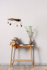 Different clothes, tree branches on table and stylish Easter decor near light wall in room