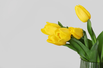 Vase with bouquet of tulips near light wall