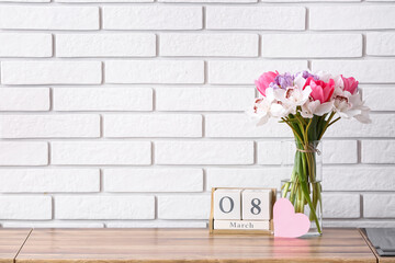 Vase with flowers, blank card and cube calendar with date 8 MARCH on kitchen counter. International Women's Day celebration