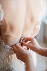Obraz na płótnie Canvas A bridesmaid helping the bride to button up her white wedding dress Morning preparation Bridesmaids hands fastening wedding dress buttons Wedding day concept Bridal dress with naked back Close up 