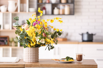 Vase with different beautiful flowers and breakfast on dining table in kitchen