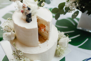 Two-tiered wedding cake with white icing close-up White wedding cake missing one piece White fresh flowers and greenery on top and in the bottom of the cake with orange stuffing Top view