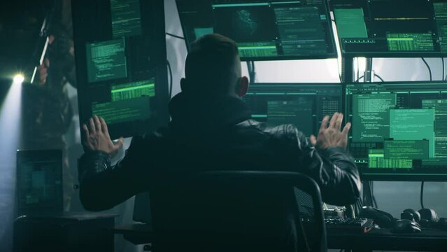 Male hacker raising hands behind head while police in uniform with guns arresting him during a cyber attack in a dark gloomy room with screens
