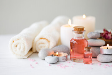 Obraz na płótnie Canvas Concept of spa treatment in salon. Natural organic oil, towel, candles as decor. Atmosphere of relax, serenity and pleasure. Anti-stress and detox procedure. Luxury lifestyle. White wooden background