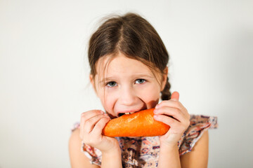 Funny caucasian girl child with carrots on a light background, vegetables and vitamins for children. Strong kid nibbles on a carrot