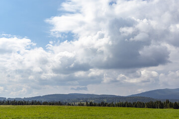 Mountain meadow in Carpathians. Countryside summertime landscape with valleys and grassy hills. Fluffy clouds on a bright blue sky