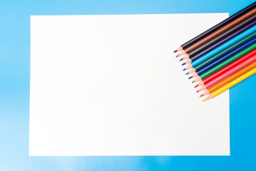 colored pencils and a white empty sheet of paper on a blue background