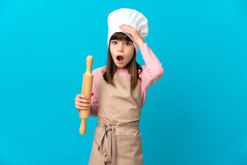 Little girl holding a rolling pin isolated on blue background doing surprise gesture while looking to the side