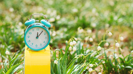 Early spring weather. Classic alarm clock with bells on nature background. Daylight saving time reminder.