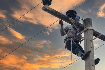 An electrician is climbing an electric pole to install and repair wires as it nears dusk.