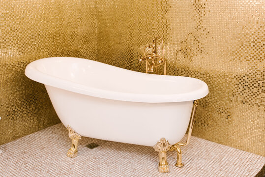 Beautiful white freestanding bathtub next to the golden tile on the wall
