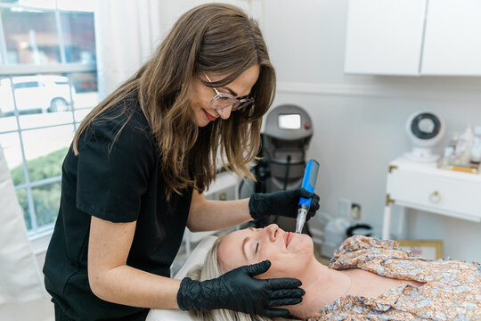 An esthtetician microneedling a spa client as she lies on a table in a health and wellness medical clinic