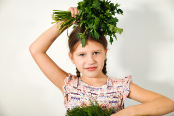 Funny caucasian girl child with bouquets of greenery on a light background, vegetables and vitamins for children. Strong child healthy food, bunches of parsley and dill