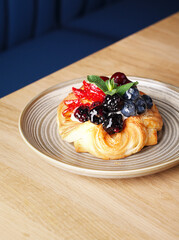 Delicious puff pastry with berries on plate on wood background. Puff pastry with strawberries, cherries, blueberries, blackberries, peaches, pineapple, cranberries and mint. Space for text. Close up.