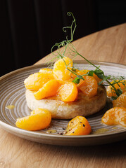 Baked camembert cheese with jam, decorated with fruits, tangerines on a plate on a wooden background. Serving baked brie cheese in a cafe and restaurant. Beautiful camembert feed Cope space. Close up.