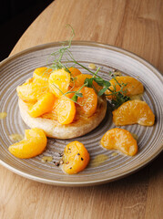 Baked camembert cheese with jam, decorated with fruits, tangerines on a plate on a wooden background. Serving baked brie cheese in a cafe and restaurant. Beautiful camembert feed Cope space. Close up.