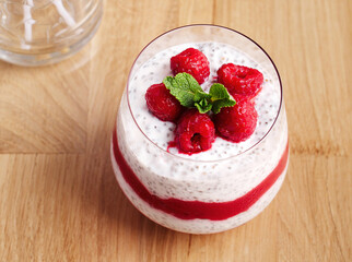 Dessert for breakfast with chia pudding, yogurt, mashed fresh raspberries, decorated with raspberries and mint leaf. The concept of healthy nutrition. Sweet dessert in a glass on a wooden background.