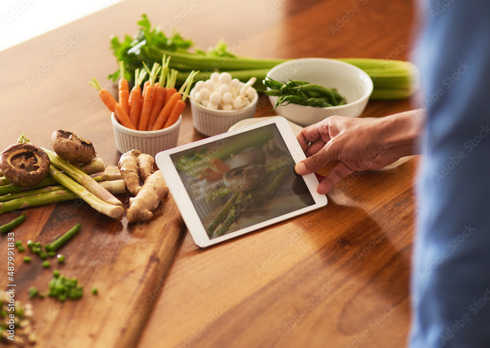 Poster recipes go paperless. cropped shot of a man using a digital tablet while preparing a healthy meal at