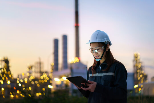 Asian Woman Petrochemical Engineer Working At Night With Digital Tablet Inside Oil And Gas Refinery Plant Industry Factory At Night For Inspector Safety Quality Control.