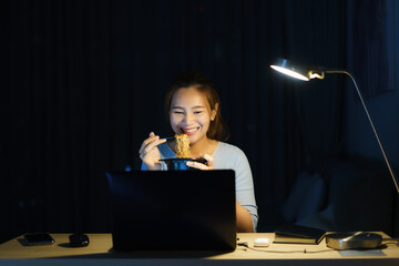 Asian freelancer smart business woman eating instant noodles while working on a laptop in the...