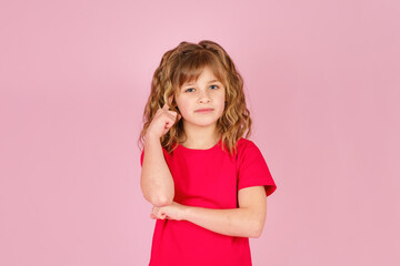 Portrait of cute curious little girl in red t-shirt isolated on pink background