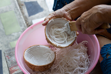 Hand of elderly woman used stainless coconut scraper for shredded coconut meat for make cooking Thai food.