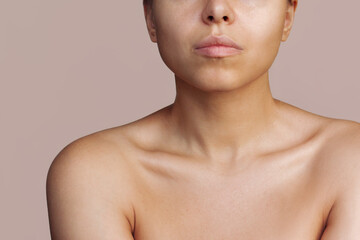 Cropped shot of a young caucasian tanned woman with a protruding collarbone isolated on a beige background. Body care, cosmetology. Soft delicate skin. Bronze skin, self-tanning, solarium. Close-up - obrazy, fototapety, plakaty