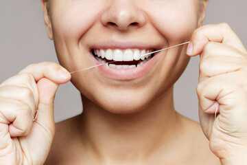 A cropped shot of a young caucasian woman flossing her teeth after meal isolated on a gray...