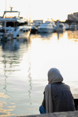 Muslim woman with hijab on her back facing the sea in the harbor
