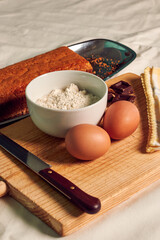 Homemade sponge cake on a white tablecloth with some ingredients: eggs, chocolate and flour.