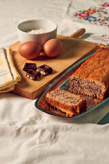 Homemade sponge cake on a white tablecloth with some ingredients: eggs, chocolate and flour
