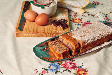 Homemade sponge cake on a white tablecloth with some ingredients: eggs, chocolate and flour