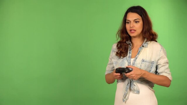 A young beautiful Caucasian woman plays a game on a console off camera with a controller in her hands - green screen background