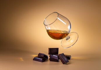 Fototapeta na wymiar Glass with cognac and pieces of chocolate on a bright background. Levitation.