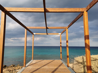 A timber-framed observation deck over the turquoise waters of the Mediterranean against a dramatic sky.