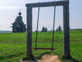 Children's swing in the village. Swing for children near a wooden church on a clear summer day.