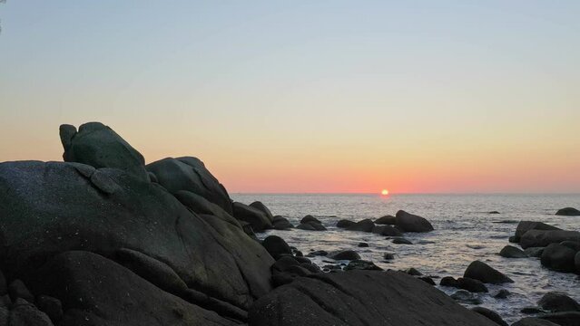 aerial view the sun going down to the horizon in sunset above the rocks..the rock beach full of stones in several size along around the island..scenery sunset above the ocean background..