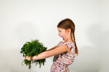 Funny caucasian girl child with bouquets of greenery on a light background, vegetables and vitamins for children. Strong child healthy food, bunches of parsley and dill