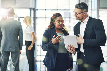 Digital planning in action. Shot of two coworkers talking together over a digital tablet in an...