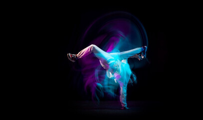 One energy young flexible sportive man dancing hip-hop or breakdance in white outfit on dark background in mixed blue neon light. Sport, art, action, moves