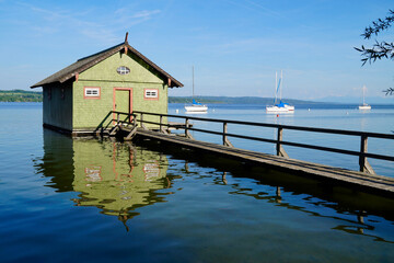 a long wooden pier leading to the colorful boat houses on lake Ammersee in the German fishing...