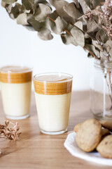 Dalgona coffee with milk, dried eucalyptus vase and cookies on wooden table.