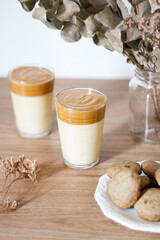 Dalgona coffee with milk, dried eucalyptus vase and cookies on wooden table.