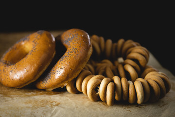 bun in the form of a ring decorated with poppy seeds and a bunch of bagels lies on parchment paper, wooden background