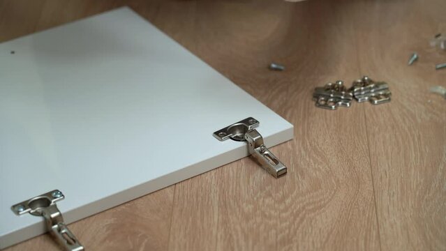 Close up of male hands screw screw with screwdriver into door hinge. Handyman assemble wooden cabinet. Furniture assembly process