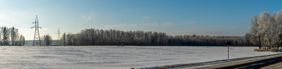 In background high-voltage electricity power pylon on snowy field with trees. High voltage poles on blue sky background.