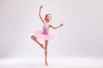 Little student ballerina dancer in a pink tutu dress dreaming of becoming a ballerina on a white...